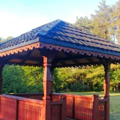 Elegancka altana z bali projekt, z rzeźbionymi elementami i drewnianym dachem, otoczona zielenią.