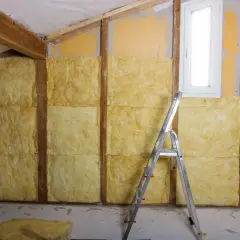 Ocieplenie ścian od wewnątrz wełną mineralną. Widać drewniane belki konstrukcyjne, okno i drabinę.