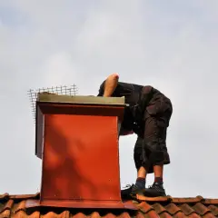 Pracownik na dachu uszczelnia komin od zewnątrz, dbając o jego prawidłowe działanie.