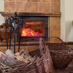 Palenisko z ogniem, obok kosze z drewnem i ozdobne wazony. To wnętrze domu, gdzie przegrody zewnętrzne budynku są dobrze izolowane, by utrzymać ciepło.