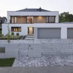 Nowoczesny dom z wysuniętym garażem, z panelami słonecznymi na dachu i eleganckim podjazdem.