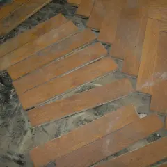 Drewniana podłoga w jodełkę, częściowo rozebrana. Widać luźne deseczki i pył. Subit, co to?