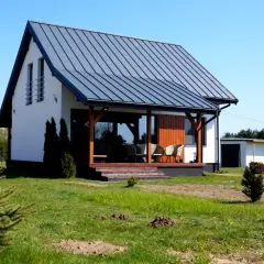 Nowoczesny dom z białymi ścianami i szarym dachem z blachy na rabek. Na werandzie meble wypoczynkowe.