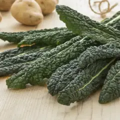 Grubo pomarszczone, ciemnozielone liście jarmużu leżą obok ziemniaków na drewnianym blacie.