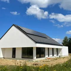 Nowoczesny dom z płyt betonowych, z panelami słonecznymi na dachu, otoczony zielenią i polnymi kwiatami.