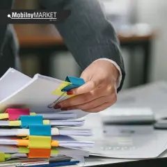 Ręce sortują dokumenty, wśród nich pozwolenie na budowę. Kolorowe spinacze porządkują stosy papierów.