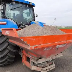Niebieski traktor z rozsiewaczem nawozu, gotowy do pracy na polskich glebach.
