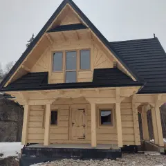 Nowy, drewniany dom w stylu góralskim z czarnym dachem, otoczony zimowym krajobrazem.
