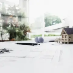 Na stole architektonicznym leży model domu, cyrkiel i plany, które wyznaczają nieprzekraczalna linia zabudowy.