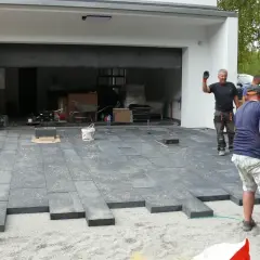 Układanie płyt na podjeździe, alternatywa dla kostki. Pracownicy montują nowoczesne, ciemnoszare płyty.