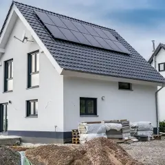 Nowy dom z panelami słonecznymi, materiały budowlane i koparki wskazują na aktywnych uczestników procesu budowlanego.