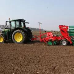 Zielony traktor z siewnikiem wykonuje wysiew jęczmienia jarego na 1 ha.