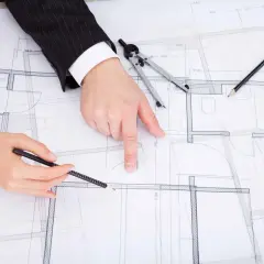Dwie osoby analizują plany architektoniczne, dyskutując o drobnych zmianach w prawie budowlanym.