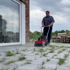 Mężczyzna używa maszyny do usuwania chwastów i mchu z kostki brukowej. To świetny sposób na utrzymanie porządku w ogrodzie.