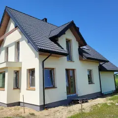 Nowy dom w stanie surowym zamkniętym, z ciemnym dachem i jasnymi ścianami, czeka na wykończenie.