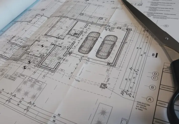 Projekt architektoniczno budowlany domu z garażem, z widokiem na plany i nożyczki.