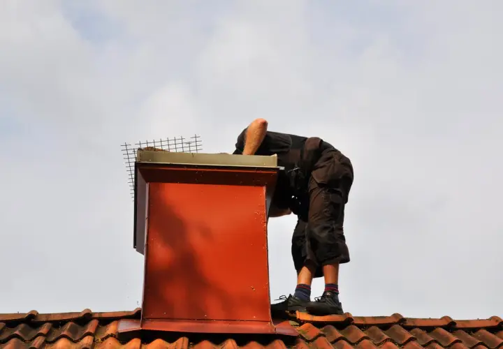 Pracownik na dachu uszczelnia komin od zewnątrz, dbając o jego prawidłowe działanie.