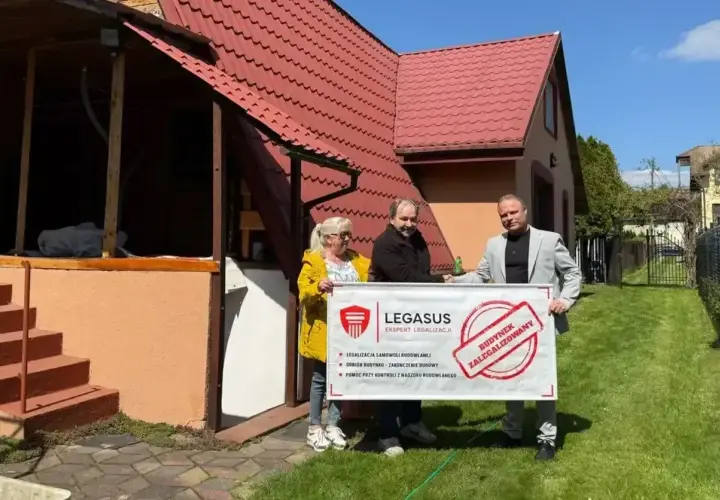 Trzy osoby trzymają baner "Budynek zalegalizowany". Pomagają w procesie jak zrobić odbiór domu po 20 latach.