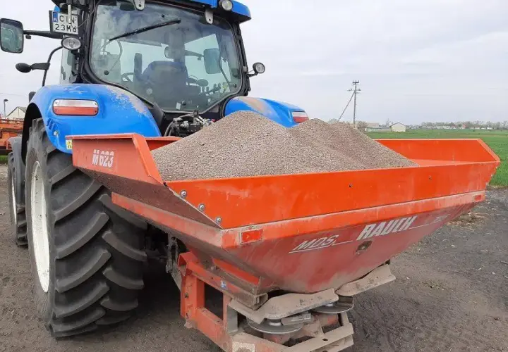 Niebieski traktor z rozsiewaczem nawozu, gotowy do pracy na polskich glebach.