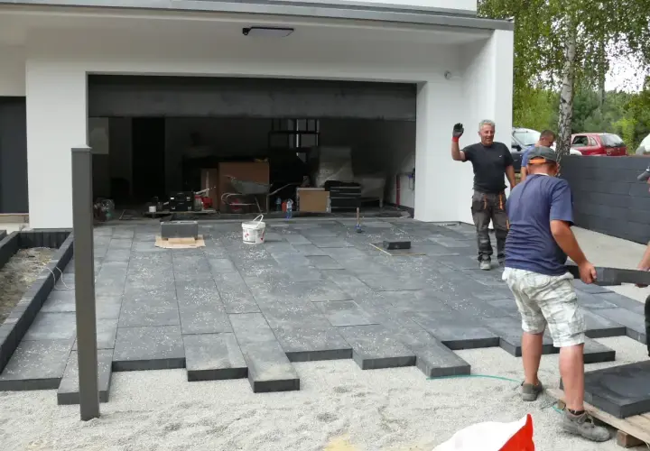 Układanie płyt na podjeździe, alternatywa dla kostki. Pracownicy montują nowoczesne, ciemnoszare płyty.