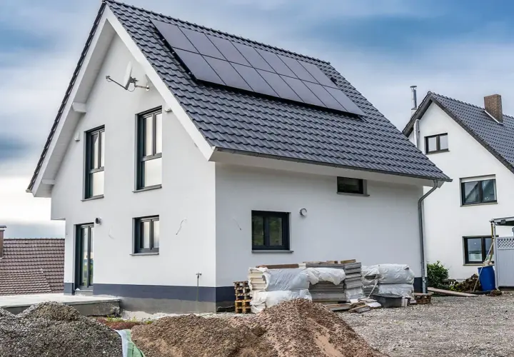 Nowy dom z panelami słonecznymi, materiały budowlane i koparki wskazują na aktywnych uczestników procesu budowlanego.