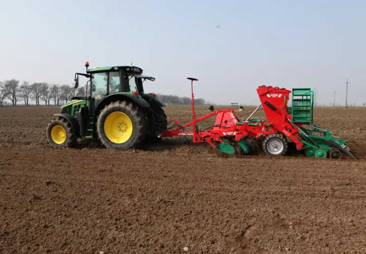 Zielony traktor z siewnikiem wykonuje wysiew jęczmienia jarego na 1 ha.