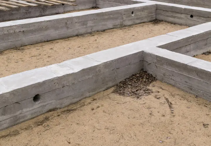 Betonowe fundamenty, czyli stan zero budynku, tworzą zarys przyszłego domu. Piasek i suche liście wypełniają przestrzeń.