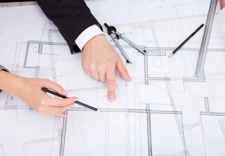 Dwie osoby analizują plany architektoniczne, dyskutując o drobnych zmianach w prawie budowlanym.
