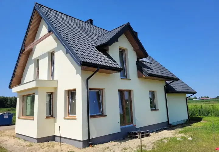 Nowy dom w stanie surowym zamkniętym, z ciemnym dachem i jasnymi ścianami, czeka na wykończenie.