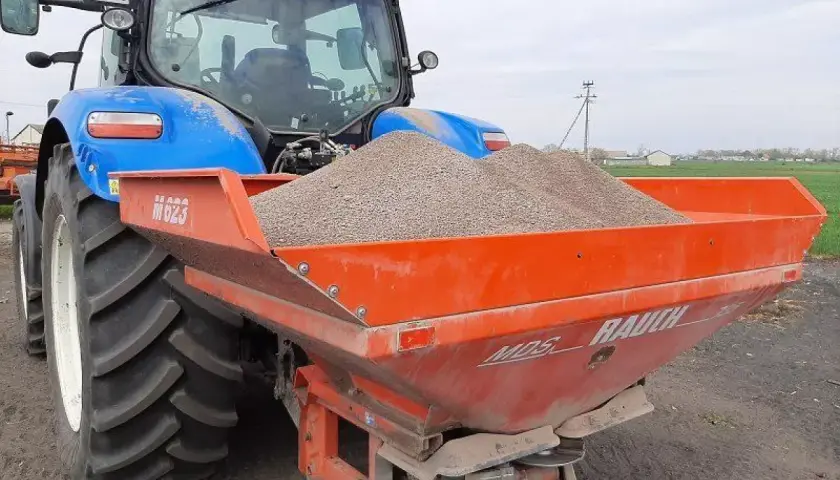 Niebieski traktor z rozsiewaczem nawozu, gotowy do pracy na polskich glebach.