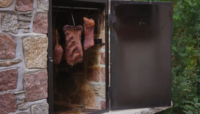 Prosta wędzarnia murowana z wędzonymi mięsami w środku.