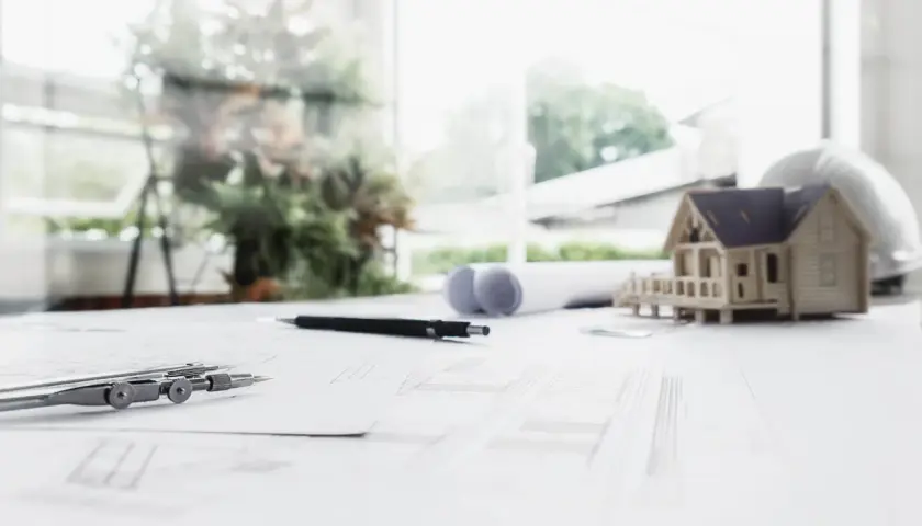 Na stole architektonicznym leży model domu, cyrkiel i plany, które wyznaczają nieprzekraczalna linia zabudowy.