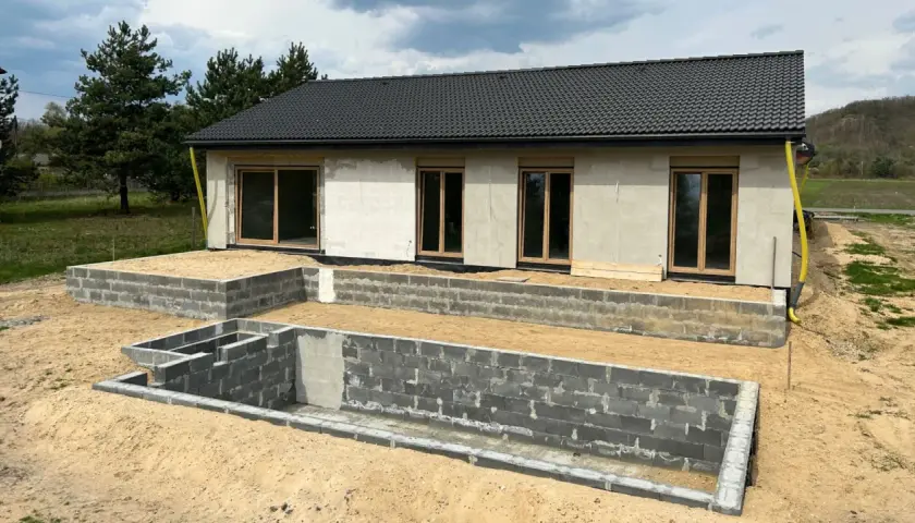 Budowa domu 3e w toku. Fundamenty i ściany parteru z bloczków betonowych, gotowe okna.