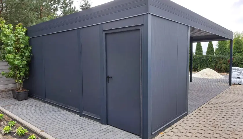 Nowoczesny budynek gospodarczy z wiatą, wykonany z ciemnoszarego metalu, z drzwiami i zadaszeniem.