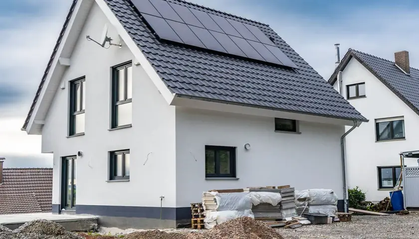 Nowy dom z panelami słonecznymi, materiały budowlane i koparki wskazują na aktywnych uczestników procesu budowlanego.