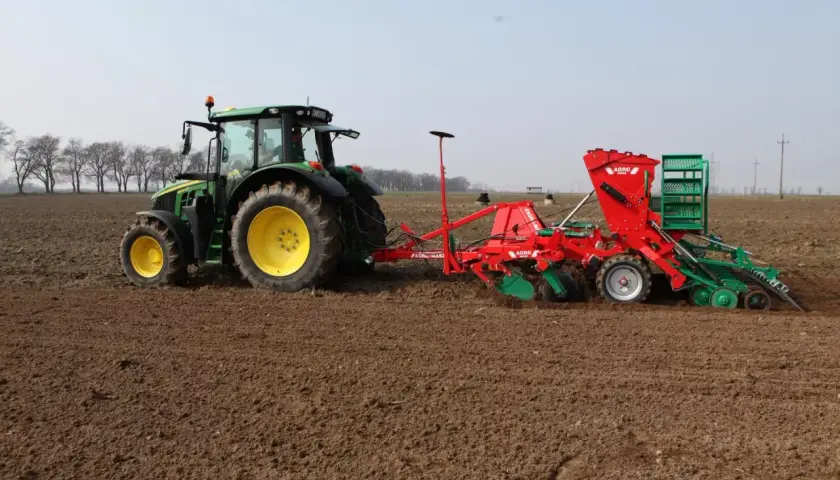Zielony traktor z siewnikiem wykonuje wysiew jęczmienia jarego na 1 ha.