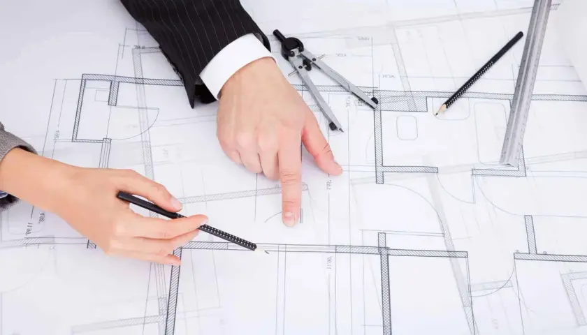 Dwie osoby analizują plany architektoniczne, dyskutując o drobnych zmianach w prawie budowlanym.