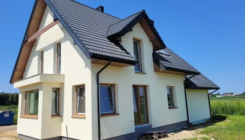 Nowy dom w stanie surowym zamkniętym, z ciemnym dachem i jasnymi ścianami, czeka na wykończenie.