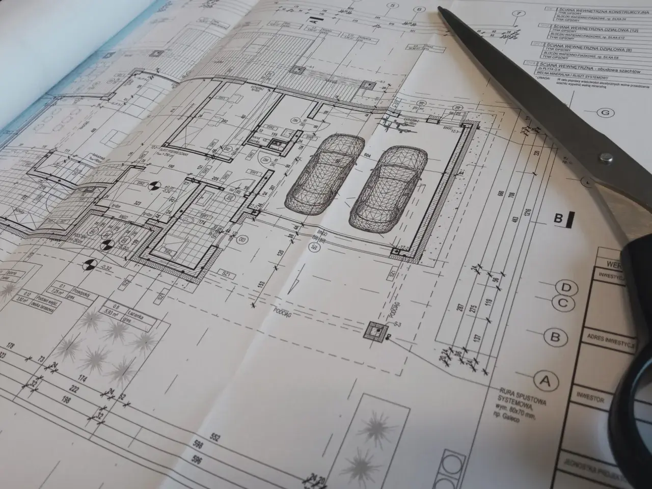 Projekt architektoniczno budowlany domu z garażem, z widokiem na plany i nożyczki.