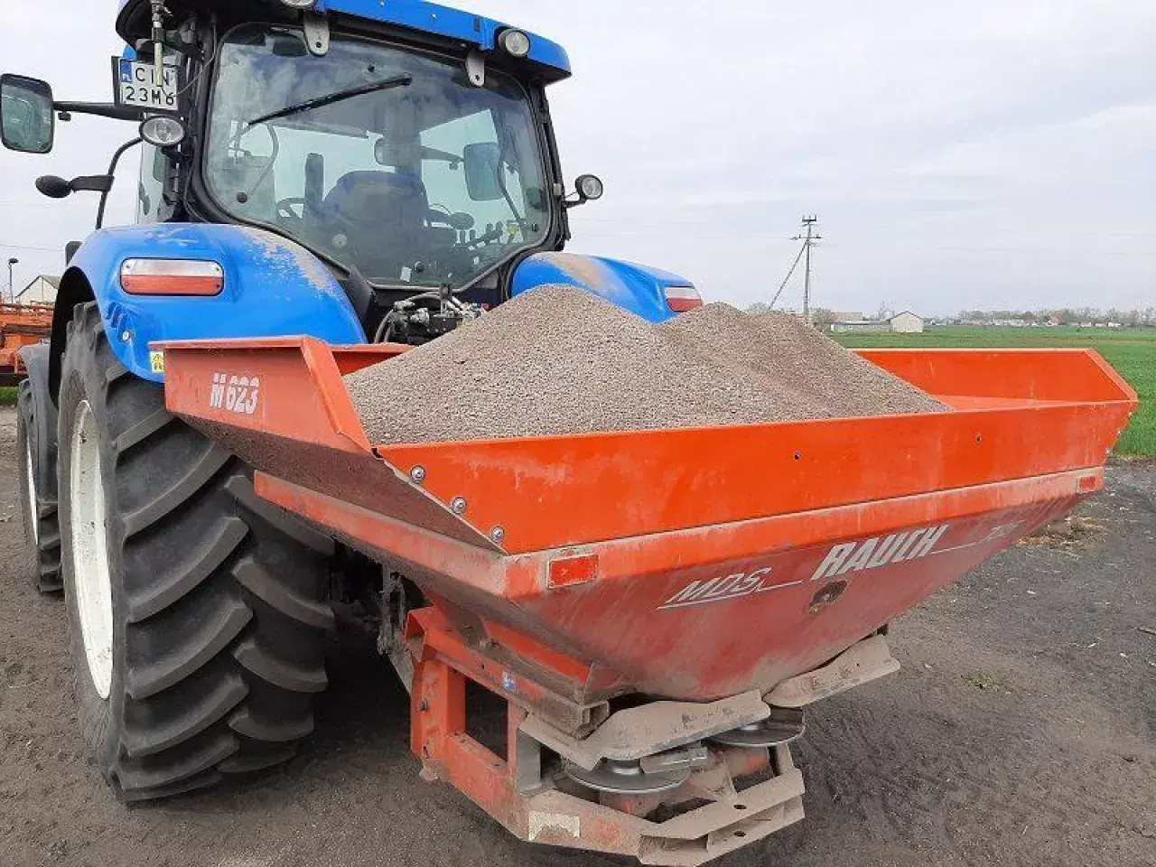 Niebieski traktor z rozsiewaczem nawozu, gotowy do pracy na polskich glebach.