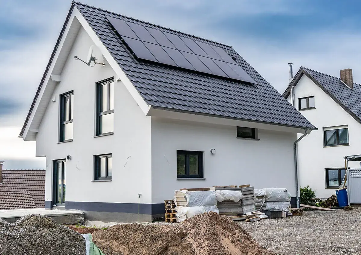 Nowy dom z panelami słonecznymi, materiały budowlane i koparki wskazują na aktywnych uczestników procesu budowlanego.