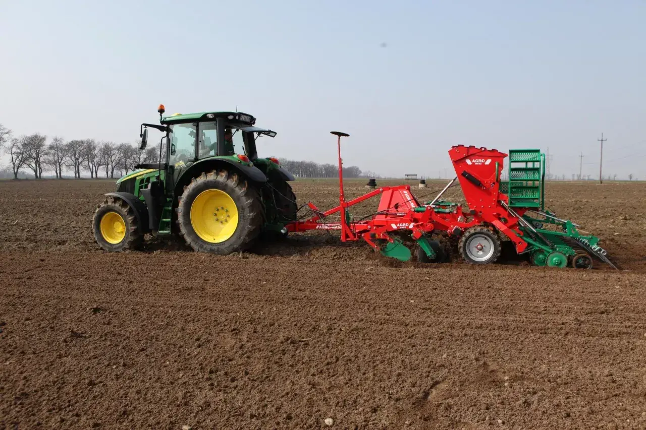 Zielony traktor z siewnikiem wykonuje wysiew jęczmienia jarego na 1 ha.