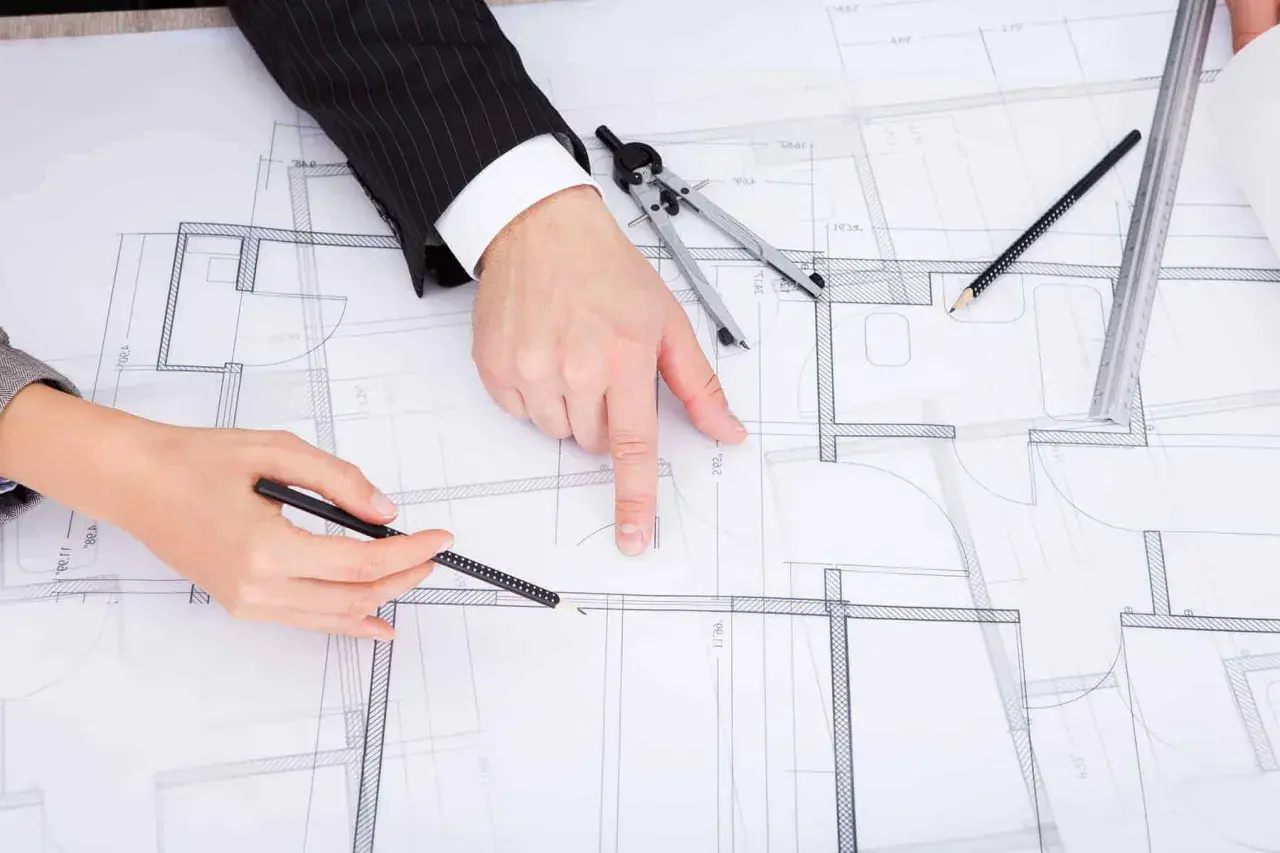 Dwie osoby analizują plany architektoniczne, dyskutując o drobnych zmianach w prawie budowlanym.