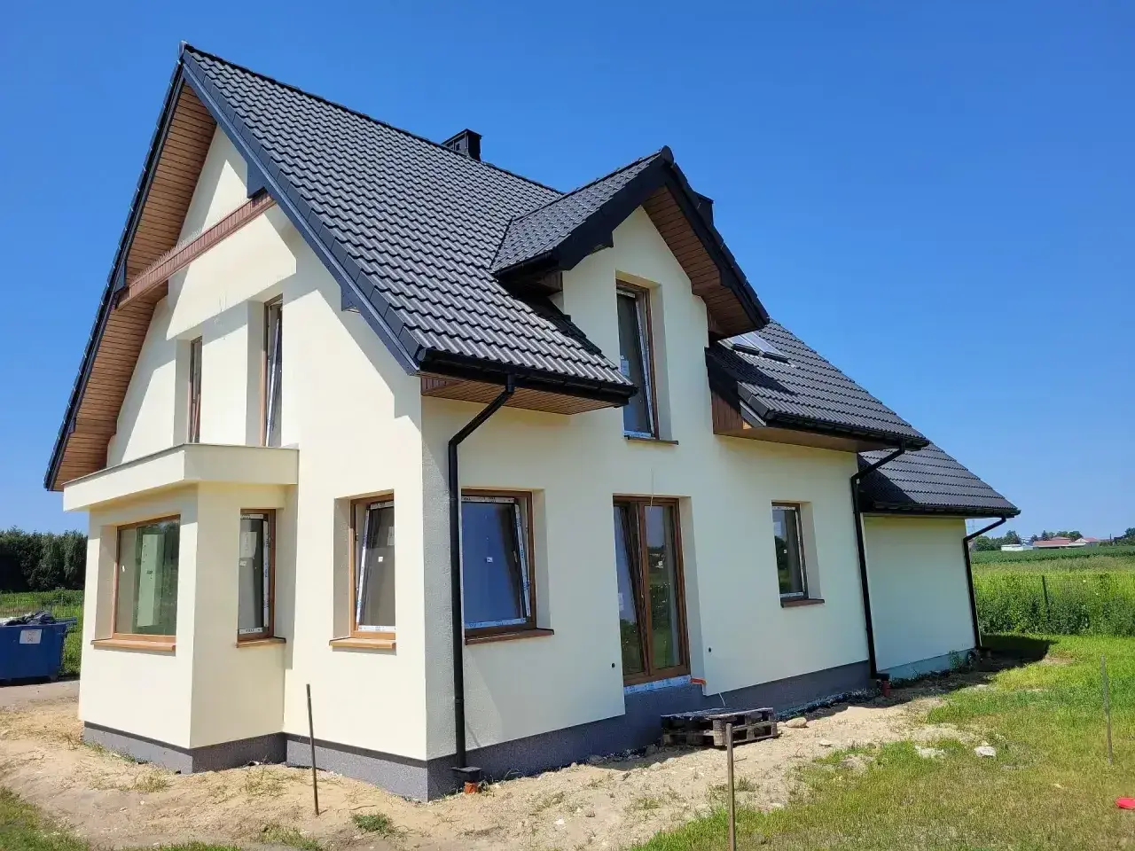 Nowy dom w stanie surowym zamkniętym, z ciemnym dachem i jasnymi ścianami, czeka na wykończenie.
