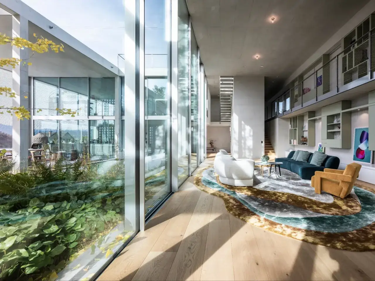 Nowoczesny projekt domu z atrium, gdzie zieleń przenika się z wnętrzem przez szklane ściany. Salon z wygodnymi sofami i designerskim dywanem.