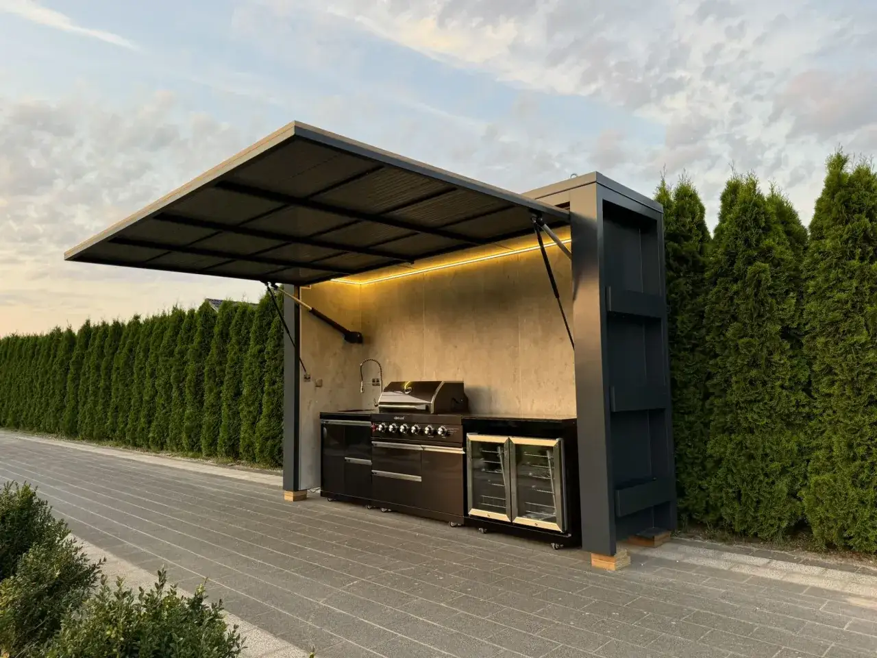 Nowoczesna kuchnia letnia projekt: grill, lodówka i zlew pod zadaszeniem. Idealne miejsce na letnie przyjęcia.