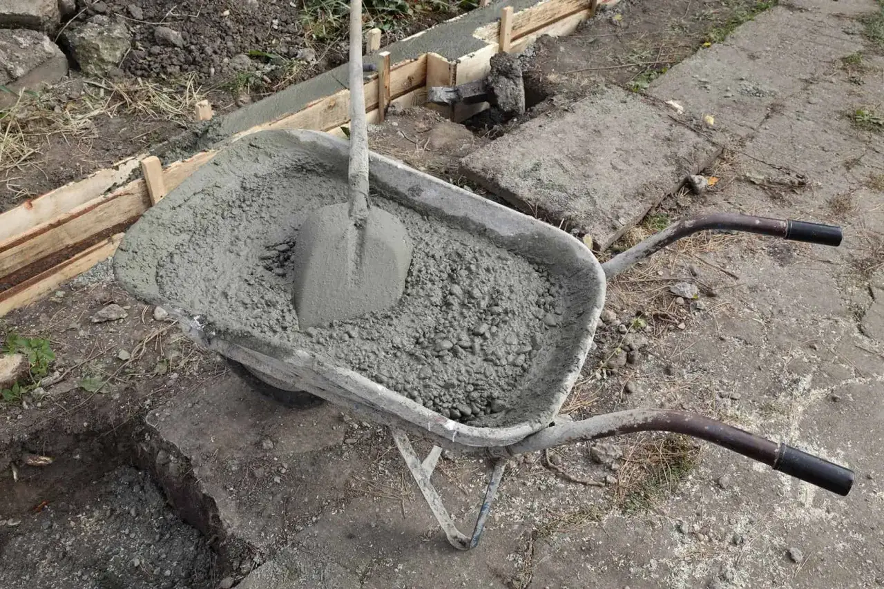 Taczka z betonem i łopatą czeka na wylanie ławy fundamentowej.