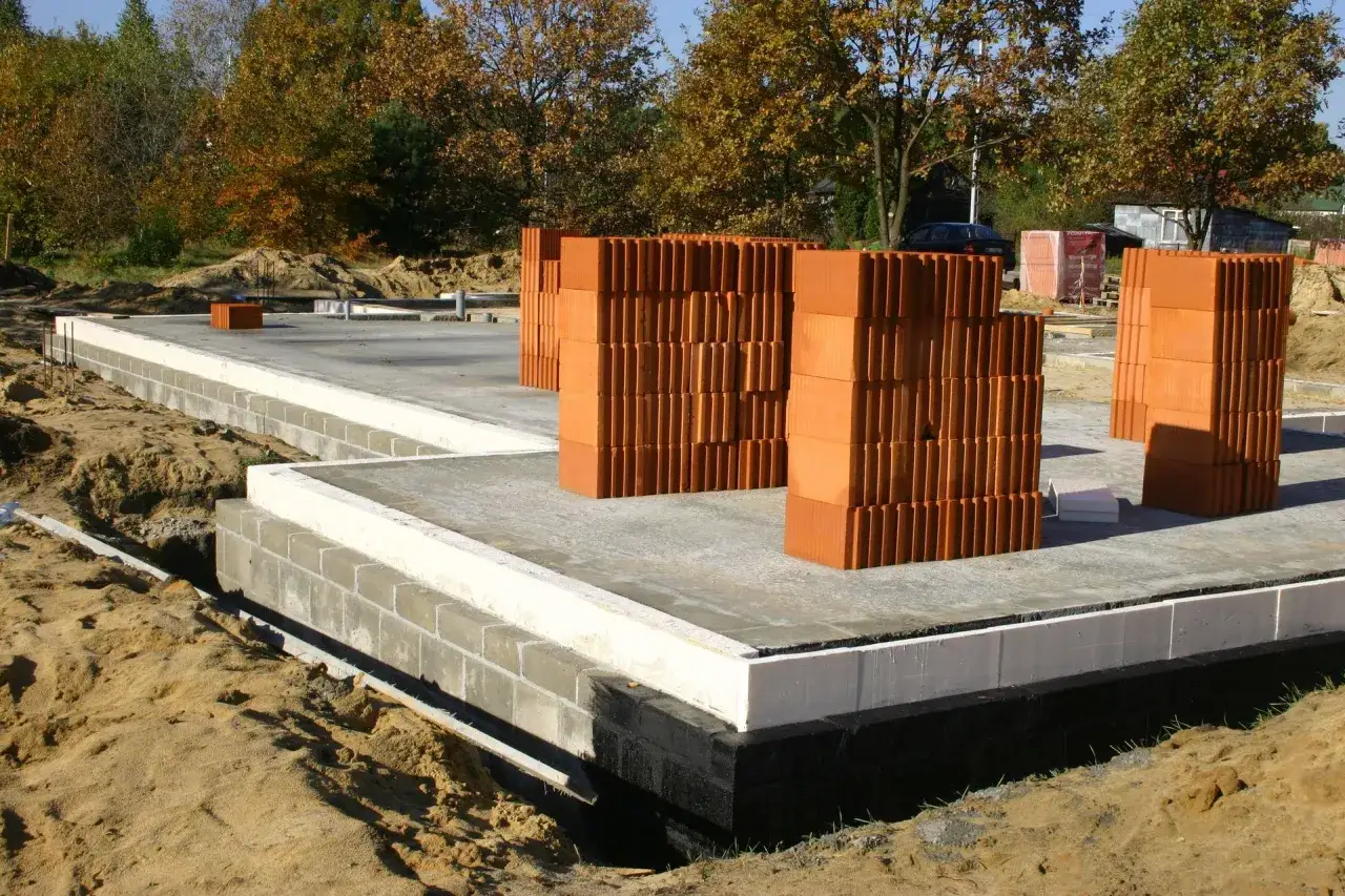 Budowa domu w toku: fundamenty z bloczków, płyta z suchego betonu, sterty pustaków.